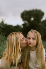 Fototapeta premium Mother gently kisses her daughter on the cheek in a tender outdoor moment