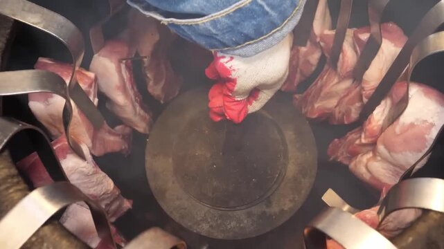 High-angle close-up footage of marinated beef steaks hanging on metal hooks inside a traditional cylindrical tandoor oven. The meat is roasting vertically over intense heat, developing a rich charred 