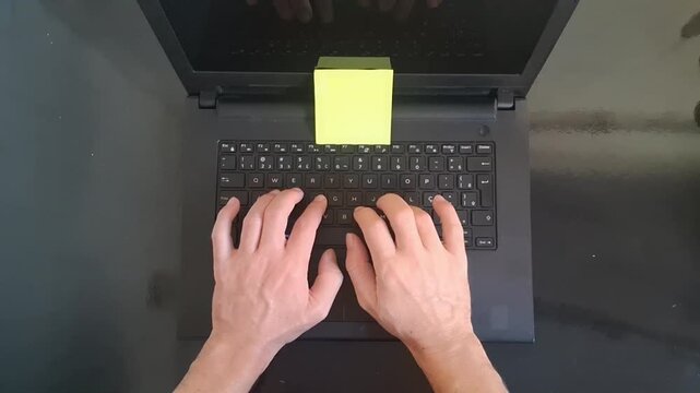 Person typing on black laptop keyboard with yellow note motion clip