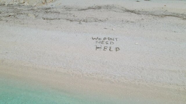 Words we don't need help written in seaweed across quiet pale sand of empty shoreline