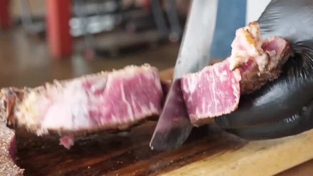 close-up of a chef wearing black nitrile gloves using a sharp professional knife to slice into a perfectly grilled, tender beef steak. The footage reveals a juicy medium-rare interior and a charred, f