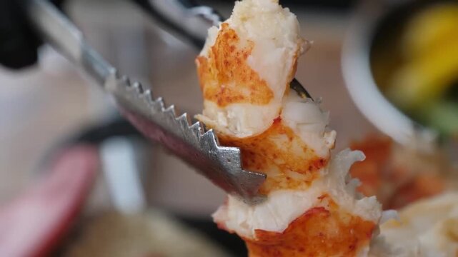 A professional extreme close-up shot of a perfectly cooked, bright red lobster tail being basted or handled during a barbecue. The juicy white meat is highlighted against the vibrant red shell, showca