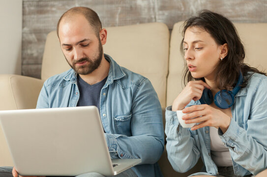 Couple uses a laptop in the living room for online shopping, relaxing together on the floor in a modern apartment interior, linking laptop browsing and home technology.
