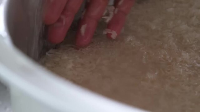 A detailed close-up shot of white rice grains inside a large pot, with a hand gently moving the grains. This footage captures the essential process of preparing, rinsing, or fluffing a staple Asian fo