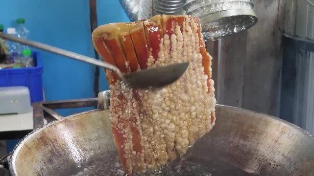 High-angle close-up shot of a chef pouring hot oil over a large slab of roasted pork belly to blister the skin. This traditional technique creates a crunchy, golden-brown crackling while keeping the m