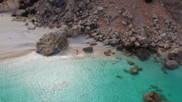 Remote Cephalonia cove with woman resting by turquoise water on peaceful rocky shore