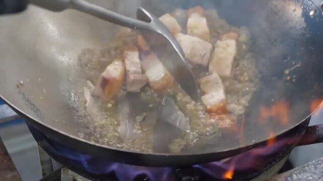 High-angle close-up of Cantonese-style crispy roast pork belly pieces deep frying in bubbling oil inside a large metal wok. The video captures the sizzling texture of the skin becoming golden and crun