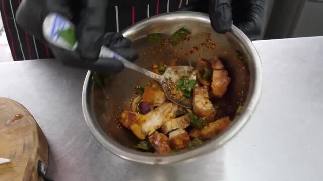Close-up footage of a professional chef wearing black nitrile gloves mixing raw beef steak with fresh green vegetables and spicy marinade in a stainless steel bowl. The preparation highlights the culi
