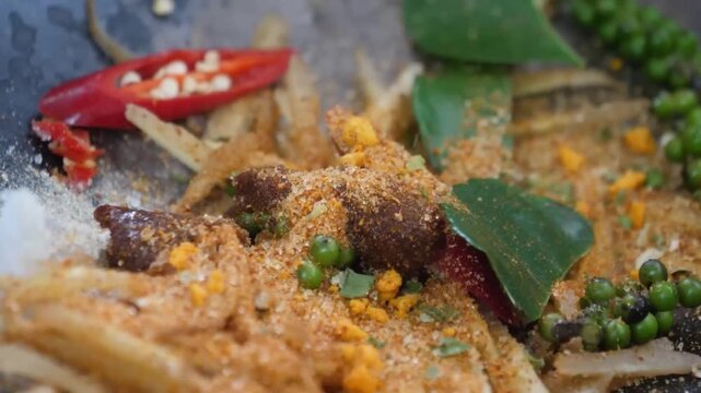 Close-up footage of a traditional spicy Thai stir-fry (Pad Cha) being prepared. The shot shows vibrant green peppercorns, kaffir lime leaves, and red chilies mixed with sizzling meat and aromatic herb