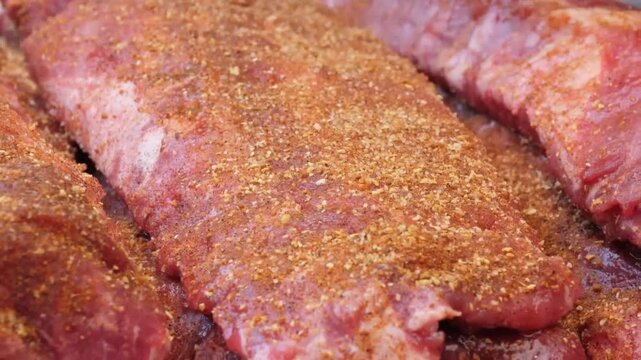 A high-quality, close-up shot of a chef wearing professional black nitrile gloves applying a savory dry rub to a fresh rack of raw pork ribs. The footage captures the detailed texture of the meat and 