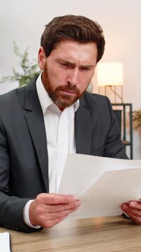 Middle-aged businessman at home office finds errors and crumples report exhales hard and calms. Freelancer guy at table opens new document edits lines fixes text and continues work with focus again.