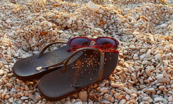 Flip flop sandals and glass on the beach with pebbles in golden sunset, summer accessories background