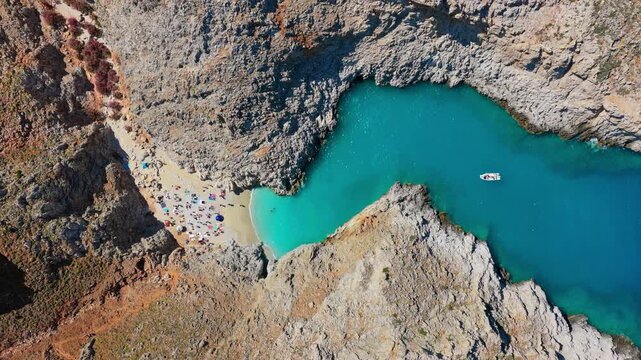 Overhead aerial drone view of a vivid turquoise cove with a small sandy beach below steep grey cliffs, Seitan Limania, Greece