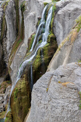 A waterfall in Yellowstone National Park cascades down a rugged, moss-covered rock face.  © Misty