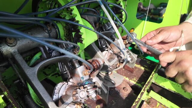 Close-Up of Rusty Baler Knotter Mechanism with Blue Grease Lubrication Tubes, Male Hands Tightening Bolt with Wrench, Farm Machinery Maintenance and Repair