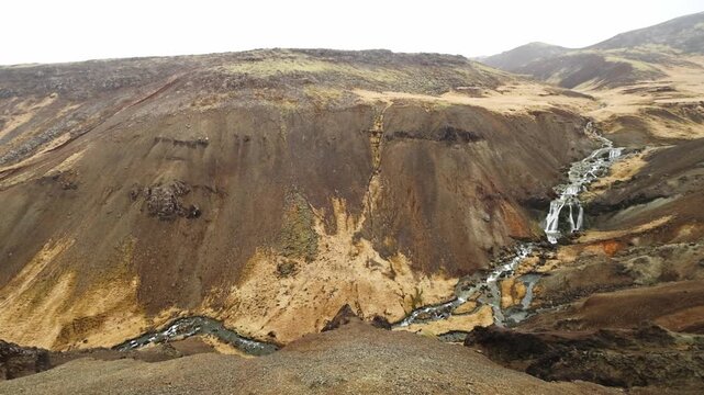 Waterfall cascading through volcanic hills on an overcast day in Reykjadalur Valley Hveragerdi South Iceland
