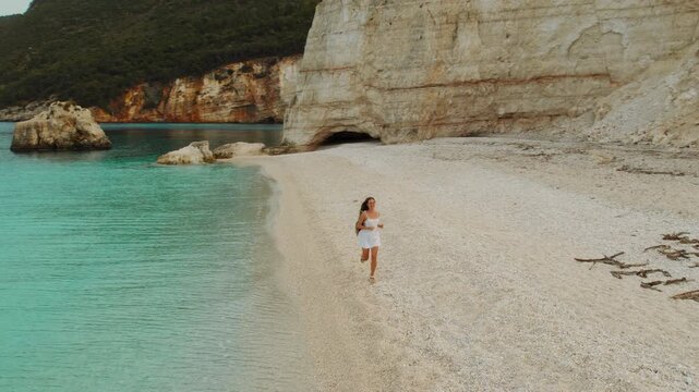 Woman jogging along peaceful Fteri beach near cliffs on coastal morning in Kefalonia Greece