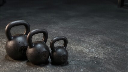 Obraz premium Three black kettlebells rest on a gritty concrete floor.