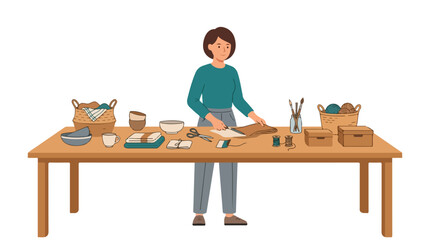 A smiling woman stands at a wooden table covered with various crafting supplies, cutting a piece of brown fabric with scissors. © Syifa