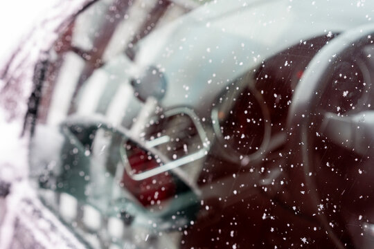 Close-up of a car windshield covered with delicate snowflakes. Through the glass, the steering wheel and dashboard are visible