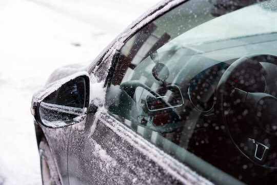 Close-up of a car driver-side window and mirror covered with snow and frost.
