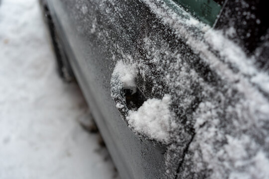 Close-up of a car door handle partially filled with snow and surrounded by frost.