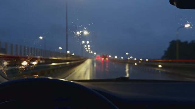 Rainy night drive through windshield with blurred bridge lights and wet road reflections