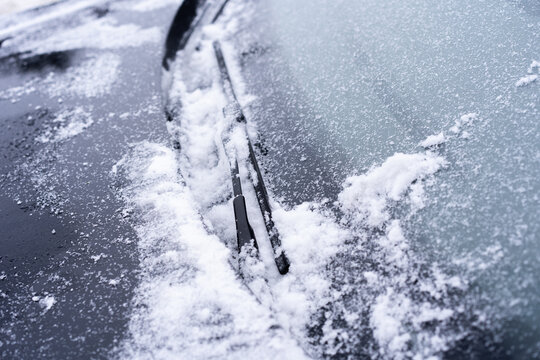Close-up of a car windshield covered with snow and ice, with wiper blades resting against the glass.