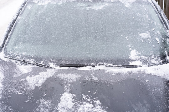Close-up of a car windshield covered with snow and ice, with wiper blades resting against the glass.