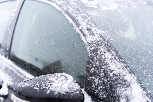 Close-up of a dark car partially covered with fresh snow and frost.