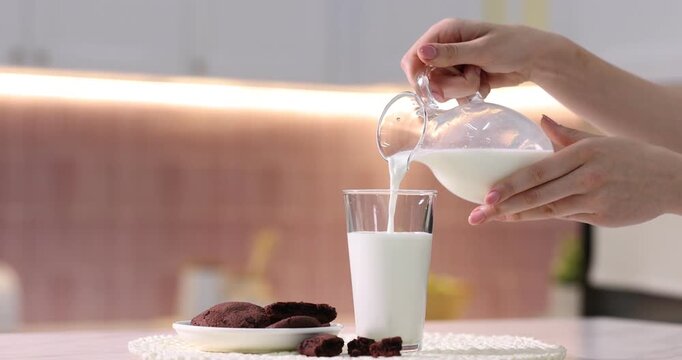 Woman pouring fresh milk into glass at table in kitchen, closeup