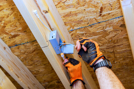 Worker installs electrical box in wooden ceiling during construction task