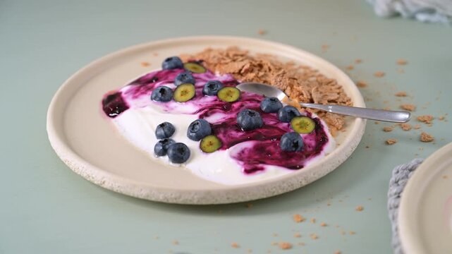 Thick yogurt swirled with vibrant berry compote is served on a textured ceramic plate with fresh berries and cereal. The soft natural side light highlights the creamy consistency and rustic details.