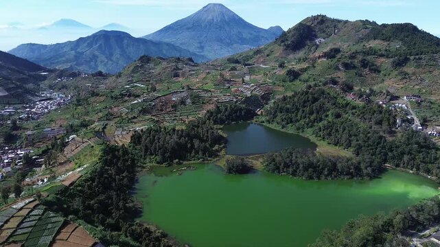 Scenic aerial landscape view of Telaga Warna and Telaga Pengilon lakes in Dieng Plateau with Mount Sindoro in the background, Central Java, Indonesia.