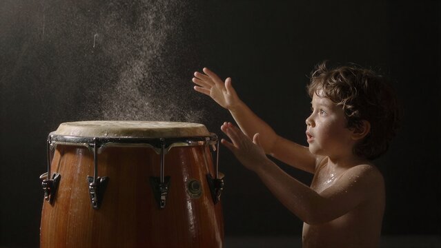 Young boy plays drum, water splashes around him in dramatic studio light.