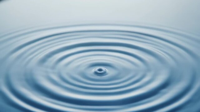 Macro view of tranquil blue water with concentric ripples radiating outward from a central drop dot