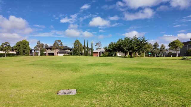 A spacious green reserve borders suburban homes under a bright blue sky in Werribee, Melbourne. A desirable green space within an established residential neighborhood in Australia