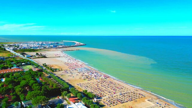 Impressive aerial truck right pan left shot of the beach between Marina Palmense and Porto San Giorgio, trees, roads, sand and parasols meet the vivid rippling waters of the Adriatic Sea under the sky