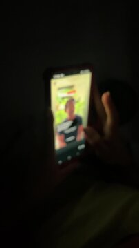 Blurred hand scrolling smartphone screen in dark room at night
