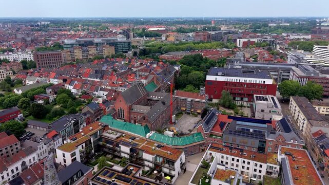 Aerial wide angle panoramic view over a modern sustainable European city block with eco green roofs solar panels and an old brick church renovation site under a summer horizon sky
