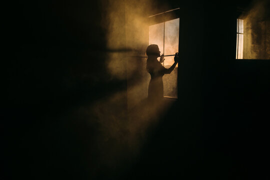 Woman Standing by Window During Sunset