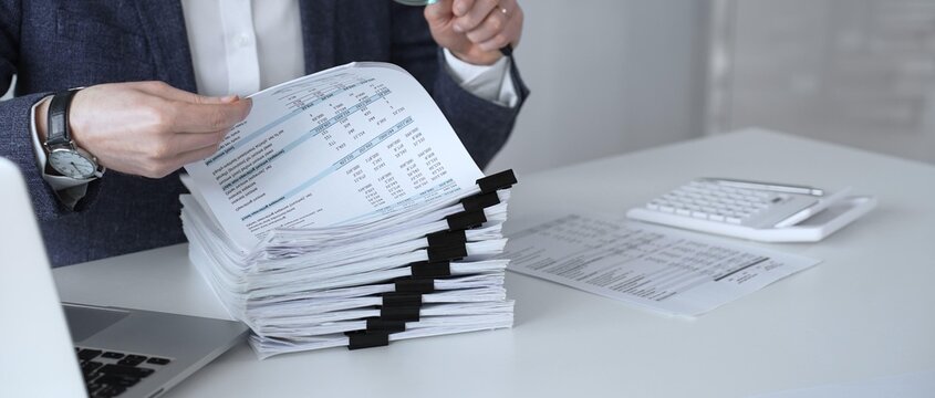 Auditor or accountant inspecting financial documents with a magnifying glass. Analyzing corporate tax records. Legal data. Invoice details. Or business reports. Audit and taxes