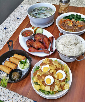 Authentic Indonesian family-style dining featuring grilled chicken, spring rolls, vegetable dishes, rice, soup, peanut salad and sambal served on a rustic wooden table.