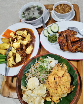 Authentic Indonesian restaurant meal featuring Javanese fried noodles, grilled chicken, Javanese beef steak, clear soup, sambal kecap and traditional side dishes.