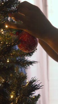 Person decorates a christmas tree with a red ornamental ball