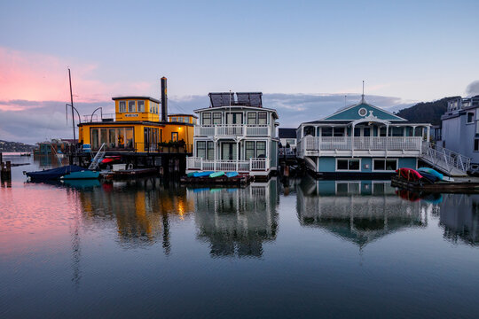 The "City of Seattle" houseboat, a historic vessel, is docked alongside other colorful houseboats on a calm body of water at dusk. The sky displays so