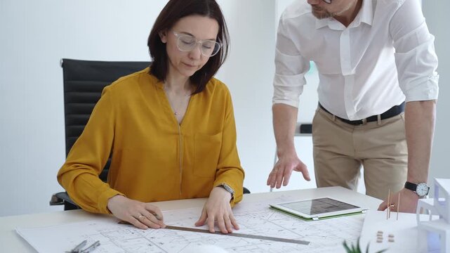 Architects collaborating on building design, reviewing blueprints, and discussing engineering plans in a modern office using a digital tablet and physical scale model