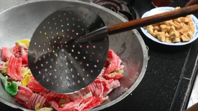 Close-up of frying colorful Indonesian crackers in hot oil. Traditional snack preparation featuring vibrant crackers, authentic local cuisine, homemade cooking, crispy texture, and delicious street fo