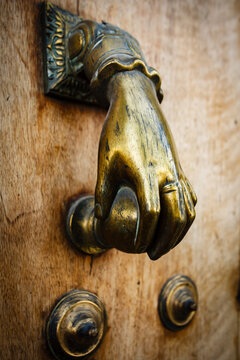 Closeup of a brass door knocker shaped like a hand turning a door knob