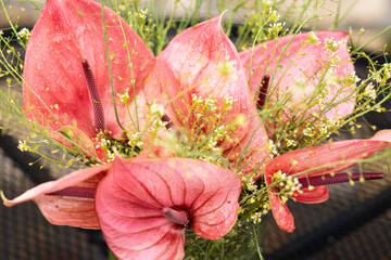 Obraz premium Elegant floral arrangement featuring pink anthurium flowers and delicate greenery in a glass vase placed on a black metal patio table.